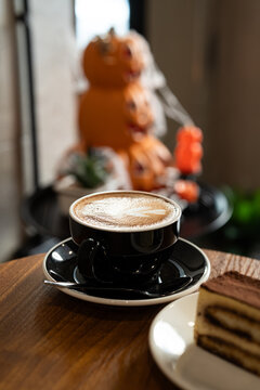 Hot coffee latte with latte art milk foam in cup mug with decor in a coffee and tiramisu cake decorated with cute edible eyeball  a theme of halloween on wood desk Halloween holiday background.