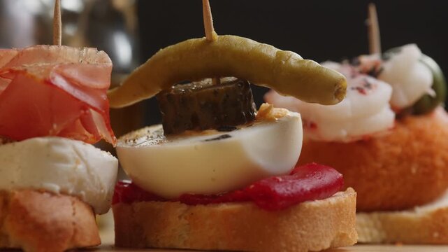 Tapas Spanish pinchos assortment, Basque pintxos with jamon iberico, tortilla, shrimp, stuffed piquillo pepper and egg on bread, traditional bar food close up