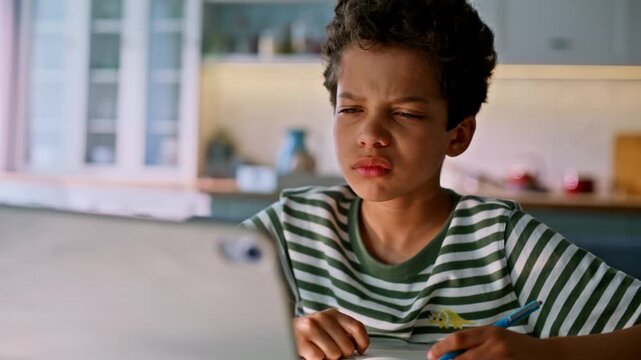 Boy studying tablet home kitchen. Concentrated child writing notes notebook.