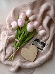 Top-down pregnancy announcement flat lay, textured soft pastel pink knitted fabric with gentle folds with a bouquet of fresh blush pink and white tulips © britaseifert