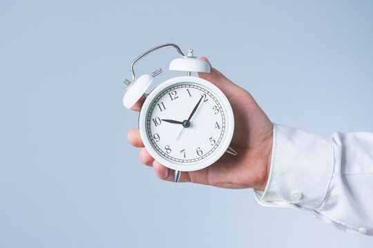 Businessman hand holding white vintage alarm clock isolated on light background. Time management, deadline pressure, work productivity, appointment scheduling and life insurance concept.
