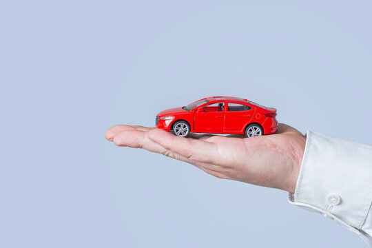 Hand holding red toy car model with copy space on light background. Car insurance, auto loan or vehicle purchase concept for automotive business.