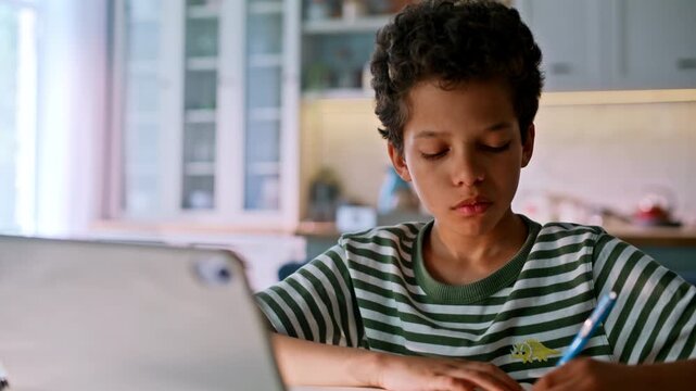 Close up boy doing homework tablet kitchen. Child writing notebook home study.