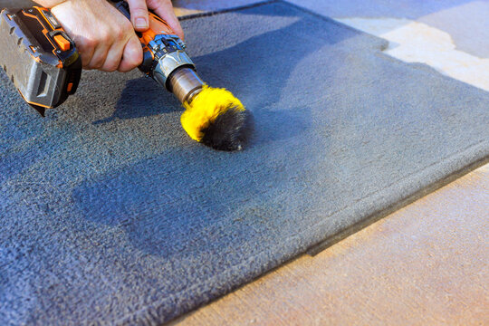 Hand guides cordless drill brush over carpet indoors during cleaning work