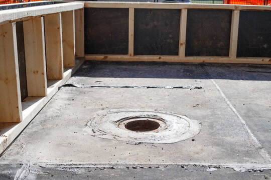 Concrete floor with floor drain on outdoor construction site. Aged drain outlet with stripped membrane and sealant residue. Waterproofing repair and drainage concept. Selective focus.