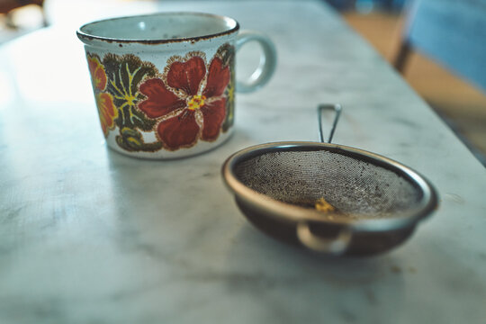Vintage Floral Ceramic Mug Next to a Tea Strainer on Marble
