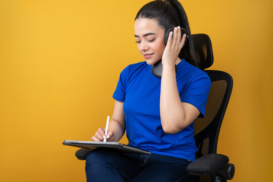 Woman wearing headphones, drawing on a tablet with a stylus against a yellow background