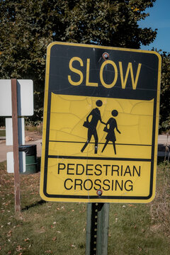 Yellow and black slow pedestrian crossing sign posted outdoors near trees and park pathway
