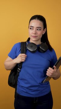 Young hispanic student holding laptop and backpack over yellow background