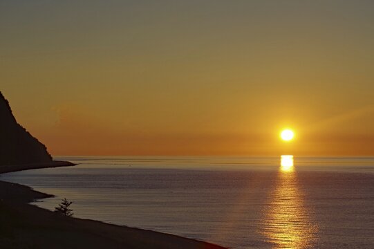 Sunset over the calm sea with a coastline and clear sky in the background, St. Lawrence River, Gaspesie, Quebec, Canada