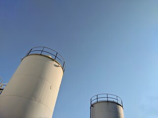 Low angle view of large industrial storage silos against a clear blue sky  © Putu