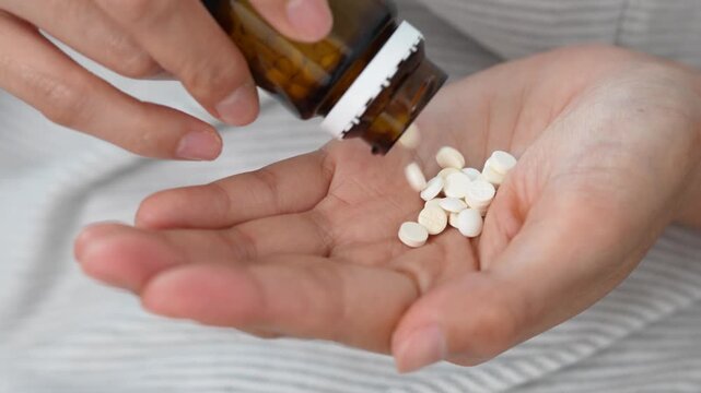 close up woman hand holding a medicine, with pours the pills out of medicine bottle. Stop drug use Taking Medication Caring for the health care medical concept.