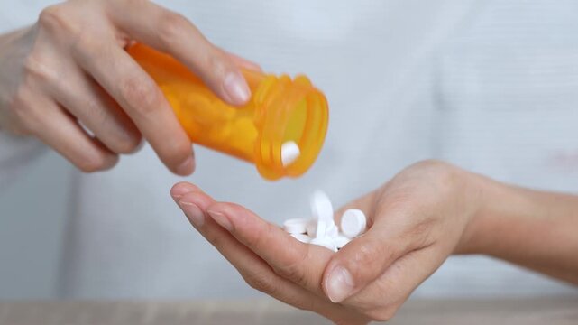 close up woman hand holding a medicine, with pours the pills out of the yellow orange medicine bottle. Stop drug use Taking Medication Caring for the health care medical concept.