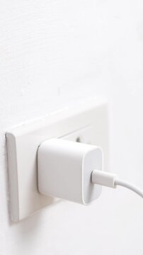 close up hand plugging adapter charge the battery with outlet socket plug and hold mobile phone on wall ,electric safety concept	
