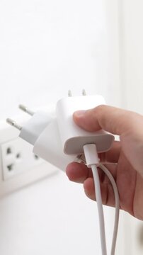 close up hand plugging adapter charge the battery with outlet socket plug and hold mobile phone on wall ,electric safety concept	