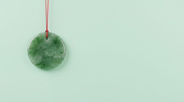 Green jade pendant, red silk cord, mint background, circular ornament with polished stone surface, hanging against pale green backdrop.