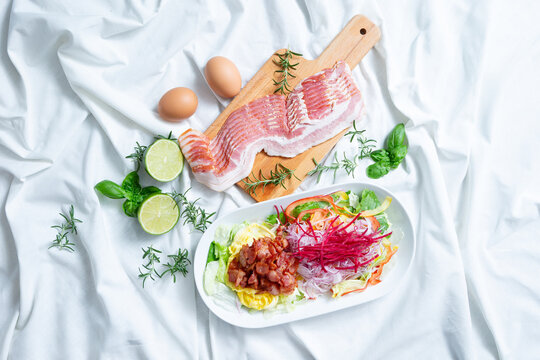 Fresh raw sliced pork belly or bacon on a wooden cutting board with eggs and limes