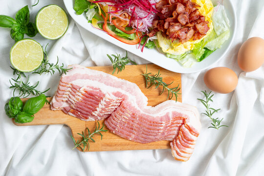 Fresh raw sliced pork belly or bacon on a wooden cutting board with eggs and limes