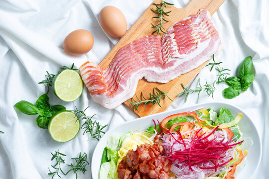 Fresh raw sliced pork belly or bacon on a wooden cutting board with eggs and limes