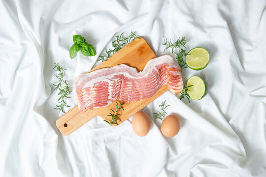Fresh raw sliced pork belly or bacon on a wooden cutting board with eggs and limes