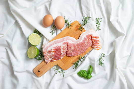 Fresh raw sliced pork belly or bacon on a wooden cutting board with eggs and limes