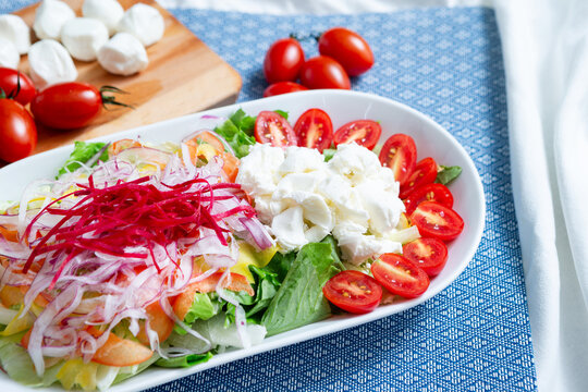 Gourmet Italian Caprese salad layout with fresh mozzarella cheese, cherry tomatoes, shredded onions, and basil on a blue placemat