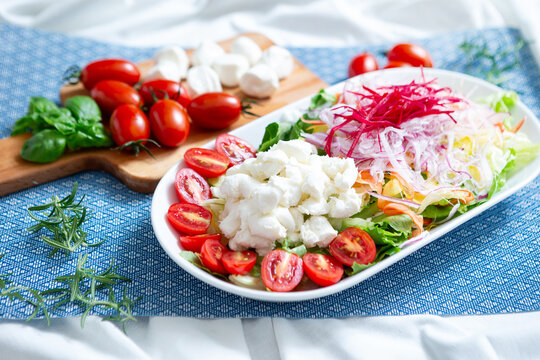 Gourmet Italian Caprese salad layout with fresh mozzarella cheese, cherry tomatoes, shredded onions, and basil on a blue placemat