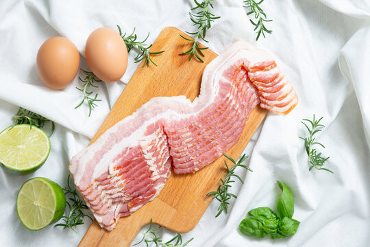 Fresh raw sliced pork belly or bacon on a wooden cutting board with eggs and limes