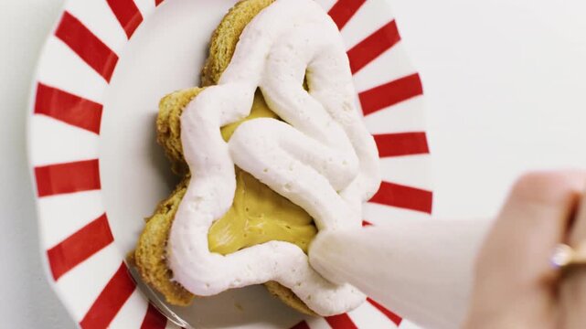 Vertical video. Treat garnishing. Dessert making. Baker hand spreading white whipped cream on gingerbread man preparing caramel cookie with piping bag.