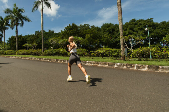 Woman running along path surrounded by lush greenery and palm trees