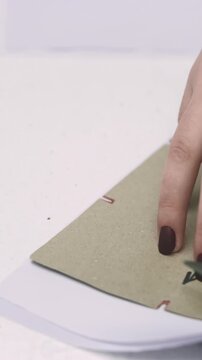 Vertical video. Cutting garment. Designer fabric. Woman working with scissors on tailoring studio table. Seamstress creating clothes with cardboard draft.