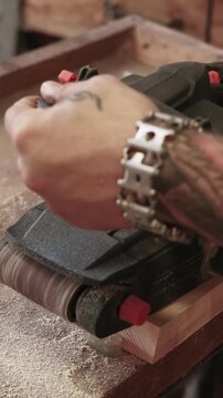 Vertical video. Woodworking process. Furniture making. Man polishing plank with handheld belt sander. Carpenter occupation with diy project workshop.