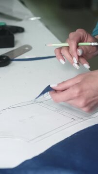 Vertical video. Sewing workshop. Apparel manufacturing. Female fashion designer hand marking with pencil paper patterns template to cutting clothing.