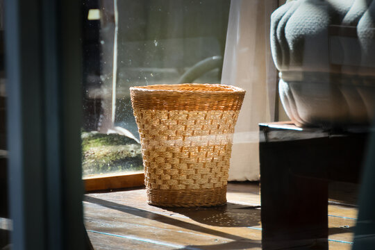 Woven basket glowing in warm sunlight beside window, with textured chair and wooden floor creating quiet rustic interior scene filled with natural light and calm atmosphere