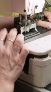 Vertical video. Clothing making. Sewing process. Tailor hand working on stitching professional machine. Woman creating buttonhole on black fabric.