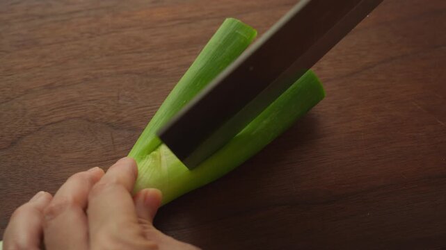Slicing a green onion lengthwise into strips on a wooden cutting board