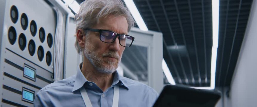 Mature IT Director Analyzing Power Consumption and Carbon Footprint Metrics on Tablet. Sustainable IT Management, Corporate ESG Strategy, Energy Efficient Servers, and Carbon Reduction Technology.