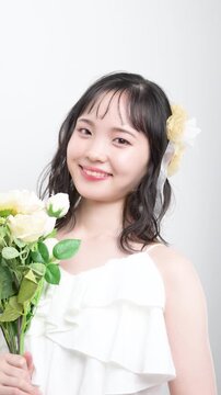 白いウェディングドレスを着てブーケを持つカメラ目線の若い20代の日本人女性の花嫁、結婚式やフォトウェディングの幸せと喜びを表現したブライダルイメージの縦動画