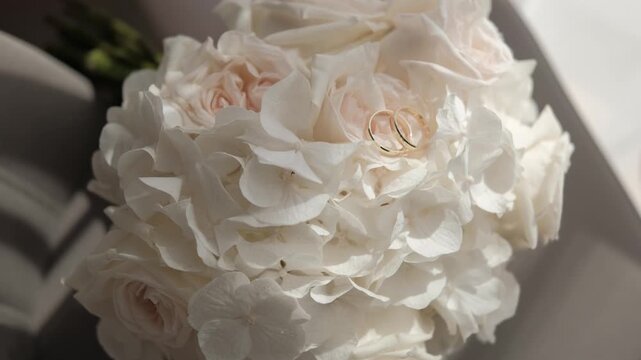 Two gold wedding rings resting gently on a beautiful bouquet of white hydrangeas and pale roses