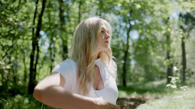 Woman meditates peacefully in sunlit forest clearing. She sits cross-legged, hands open, eyes closed. Serene expression shows calm focus and inner peace. Scene ideal for wellness, mindfulness