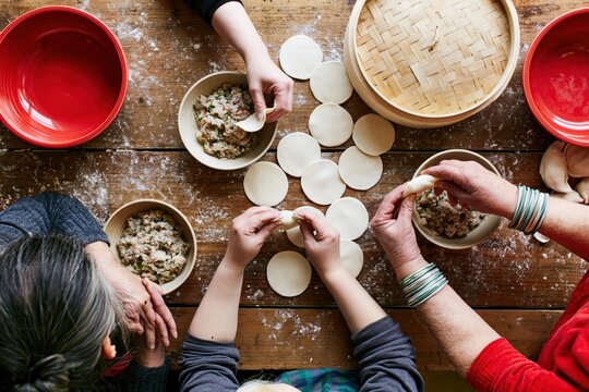 Overhead view of three generations of hands filling and pleating dumplings with round wrappers on a rustic flour-dusted table