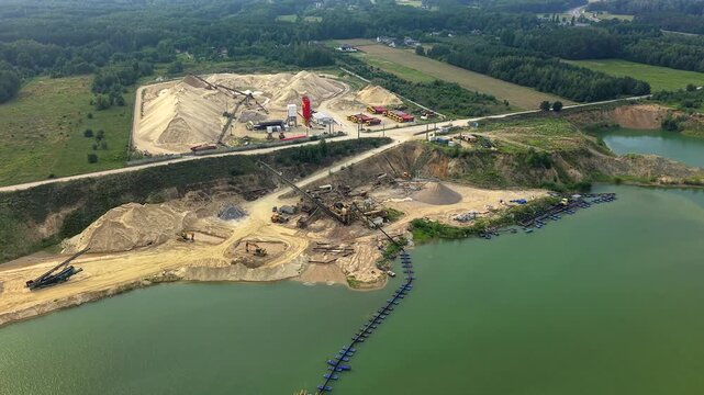 Panoramic aerial view of a large open pit sand and gravel mine. Industrial machinery and a dredging pipeline extracting materials from the water