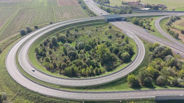 Aerial view of a circular highway interchange on the A58 motorway in northern Italy, with light traffic moving through connecting roads and surrounding transport infrastructure