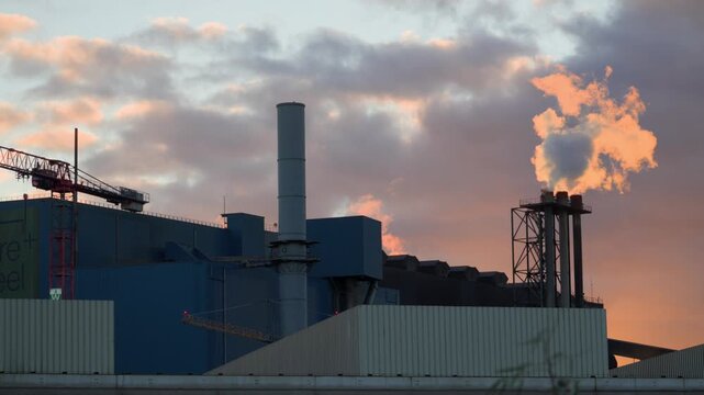 Industrial facility and chimneys release steam beneath warm clouds at autumn sunset in France