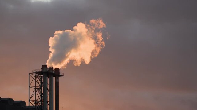 Close of a large steam plume rising from industrial chimneys against a warm autumn sky in France