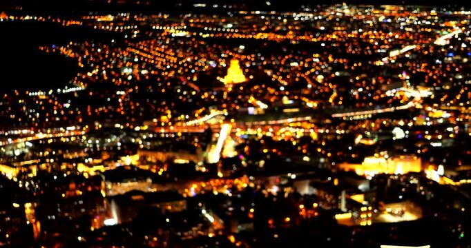 Blurred city lights come into focus around illuminated Holy Trinity Cathedral and a river bridge above dense nighttime buildings in Tbilisi