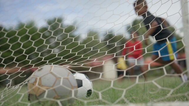 Soccer Ball Inside Goal Net with Young Football Player on Outdoor Field