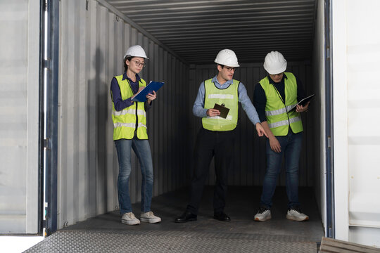 Professional logistics team and quality control inspectors in hardhats and safety vests checking empty freight container before export shipping delivery