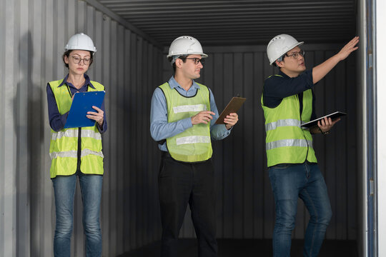 Professional logistics team and quality control inspectors in hardhats and safety vests checking empty freight container before export shipping delivery