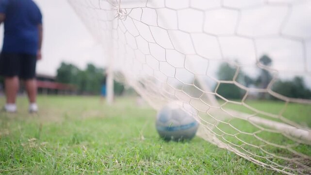 Soccer Ball Inside Goal Net on Green Grass Field with Player in Background